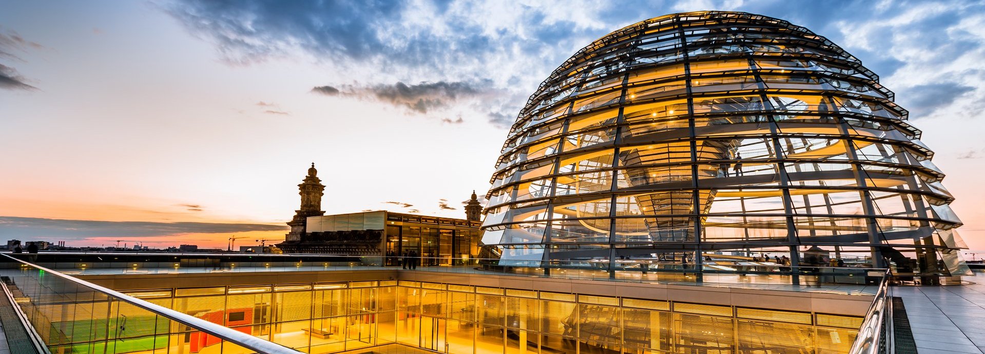 Beschreibung: Gelb beleuchtete Kuppel und innere Gänge des Bundestags vor dunkelblauem wolkigem Himmel