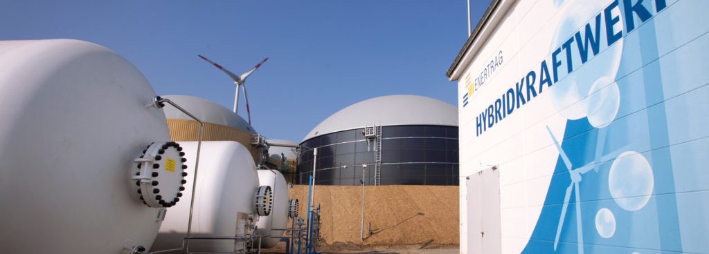 Beschreibung: Enertrag-Hybridkraftwerk mit blauem Himmel und Windrad am Horizont