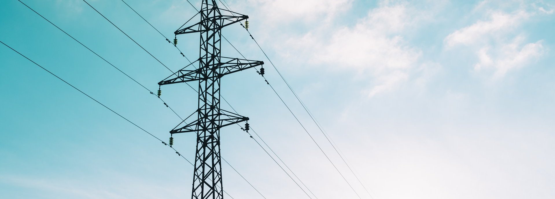 Tiefe Ansicht auf Strommast vor hellblauem leicht bewölktem Himmel