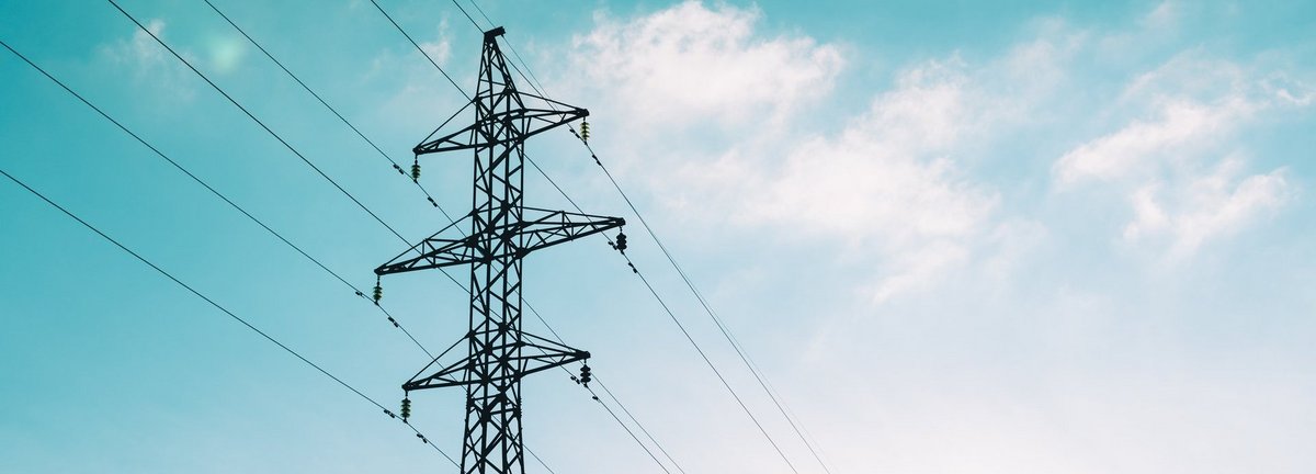 Tiefe Ansicht auf Strommast vor hellblauem leicht bewölktem Himmel