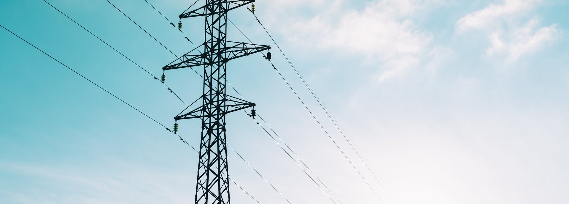 Tiefe Ansicht auf Strommast vor hellblauem leicht bewölktem Himmel