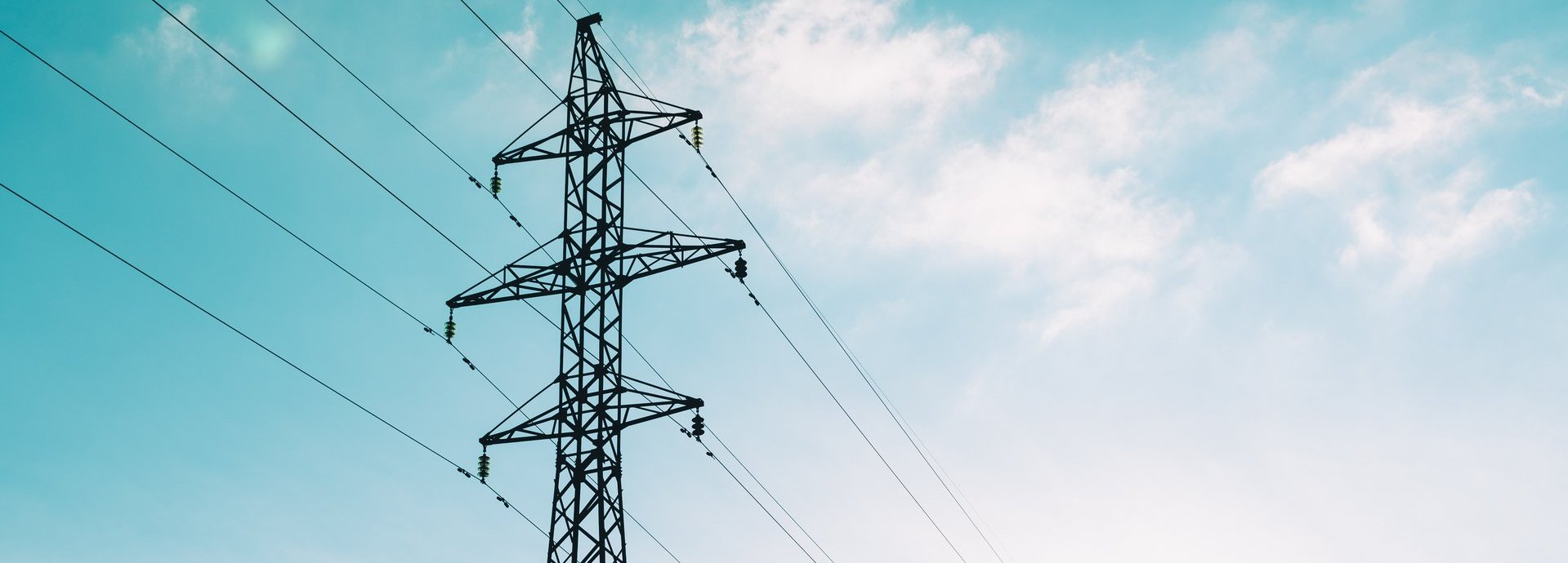Tiefe Ansicht auf Strommast vor hellblauem leicht bewölktem Himmel