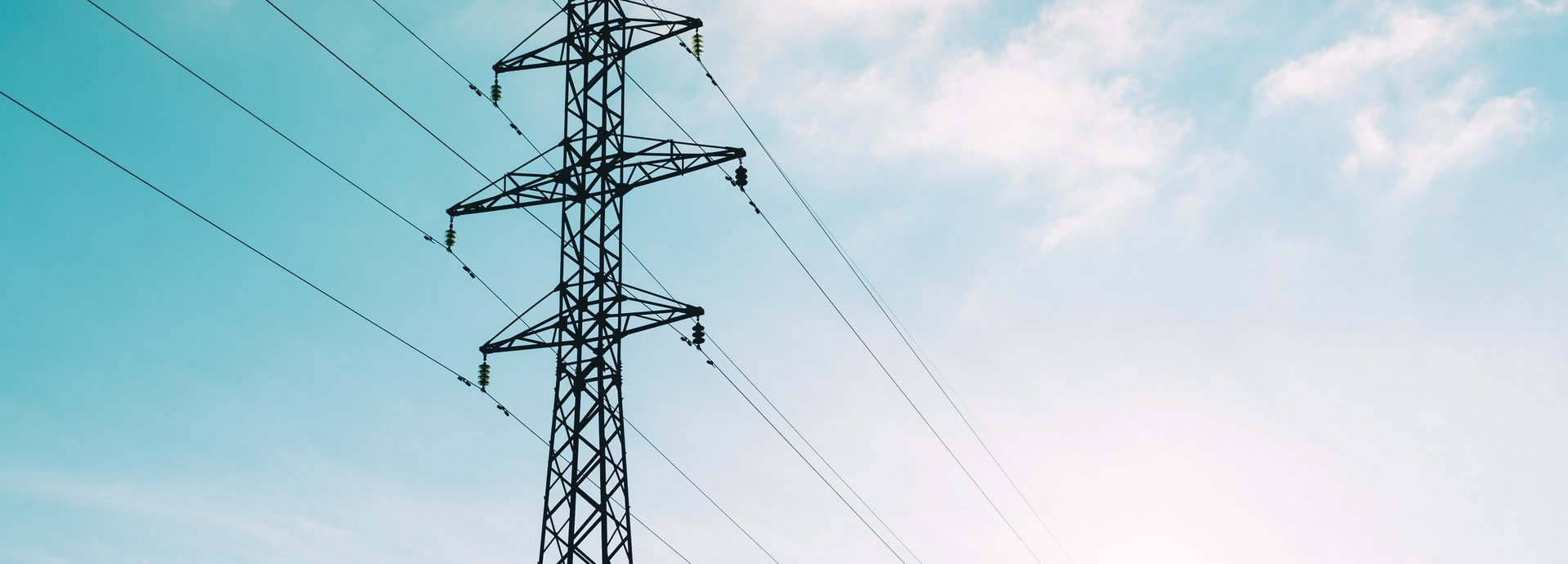 Tiefe Ansicht auf Strommast vor hellblauem leicht bewölktem Himmel