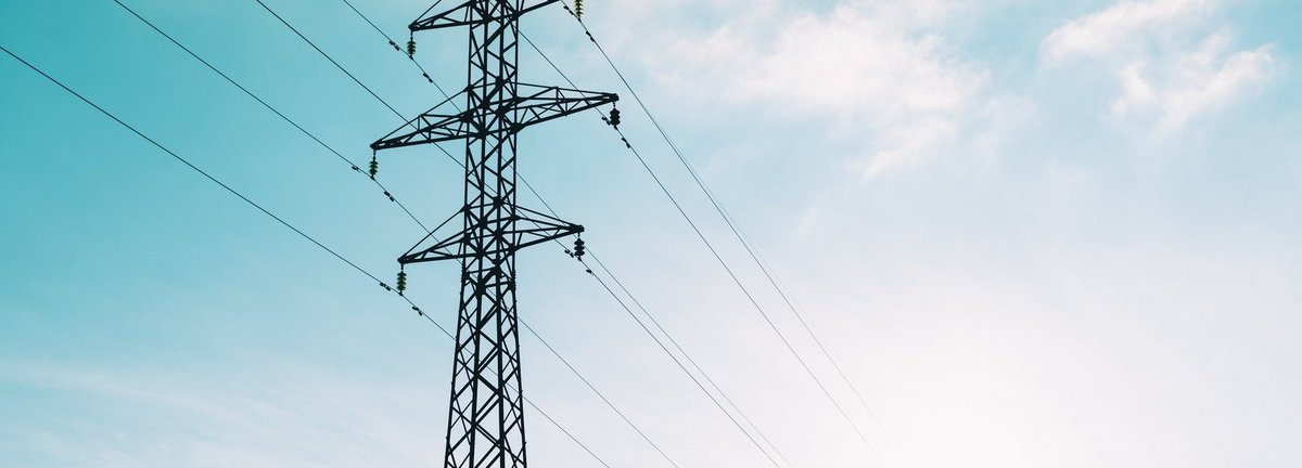 Tiefe Ansicht auf Strommast vor hellblauem leicht bewölktem Himmel