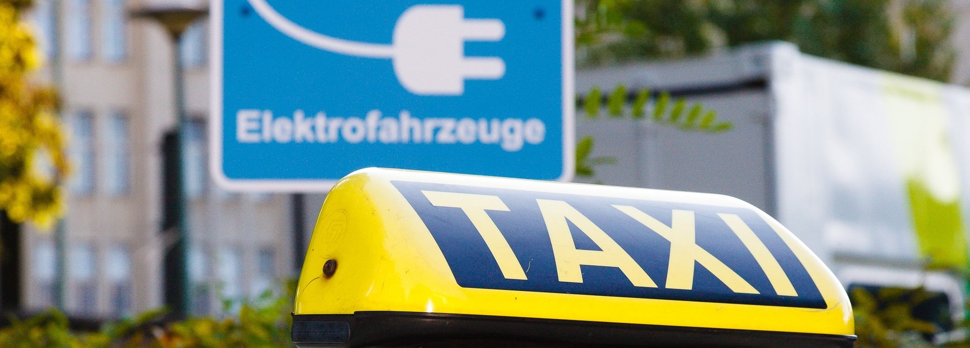 Straßenschild Reserviert für Elektrofahrzeuge in der Stadt, davor ein Taxizeichen