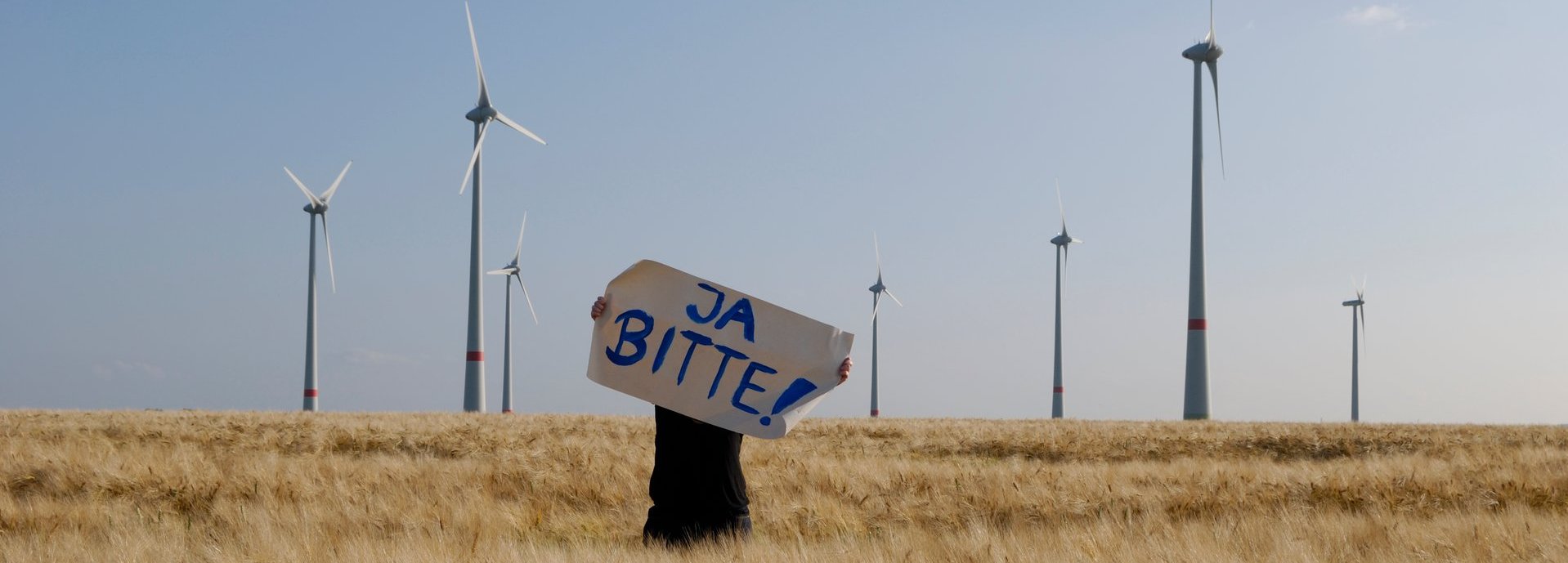 Mensch mit "Ja Bitte"-Schild vor einem Windpark