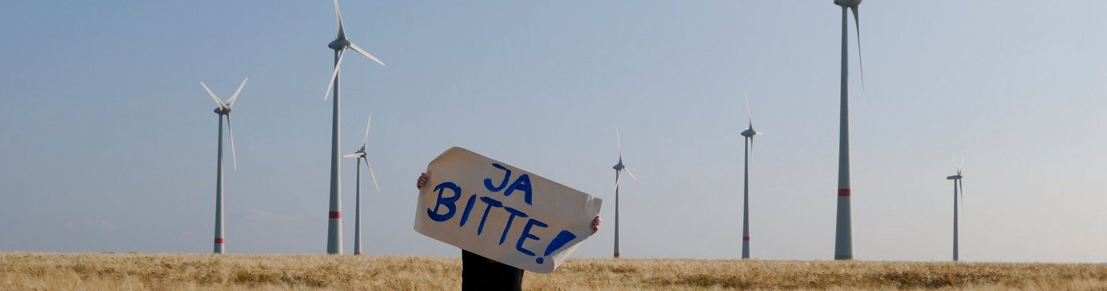 Mensch mit "Ja Bitte"-Schild vor einem Windpark