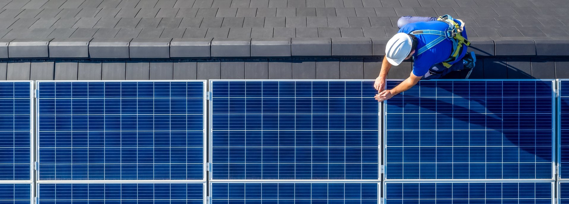 Arbeiter mit blauem Shirt montiert Solarkollektoren auf einem Hausdach