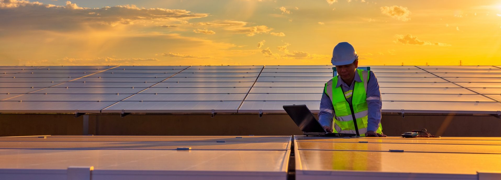 Ingenieur mit Laptop an Sonnenkollektoren auf dem Dach bei Sonnenuntergang, ein Ingenieur, der auf einer Photovoltaikfarm arbeitet. Eco-Technologie für elektrische Energie