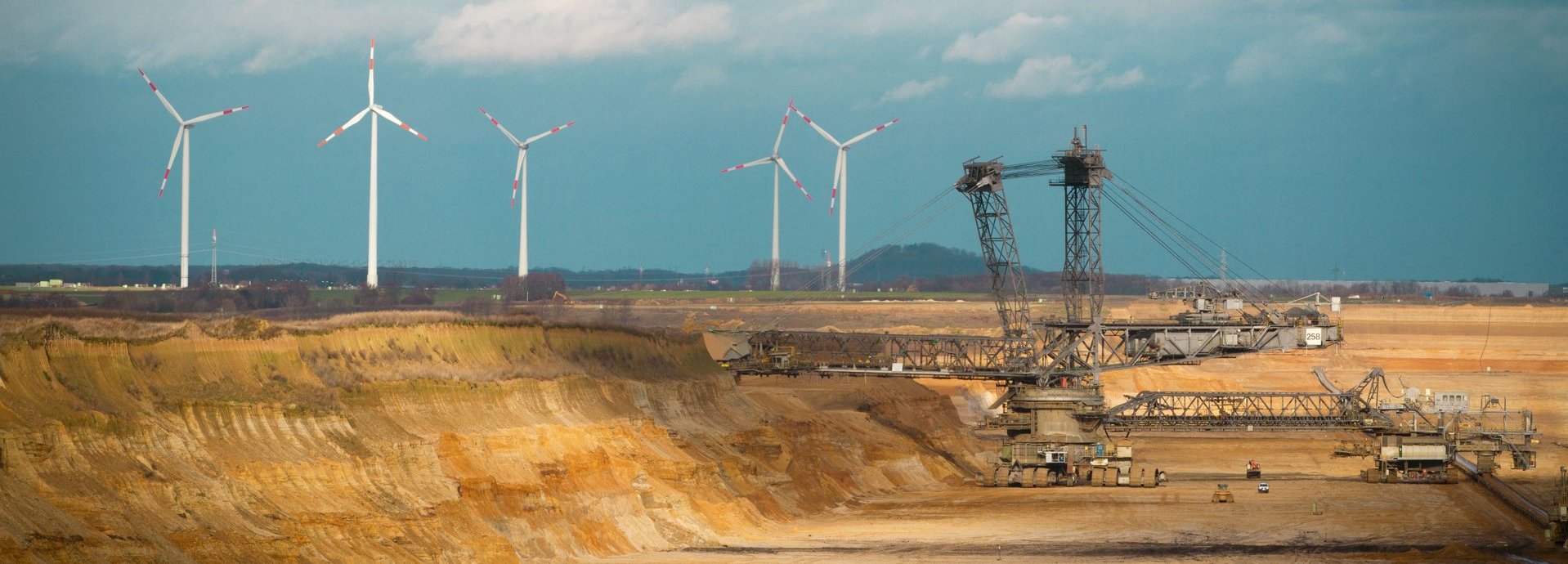 Kohlegrube mit Windrädern am Horizont vor wolkenbehangenem Himmel
