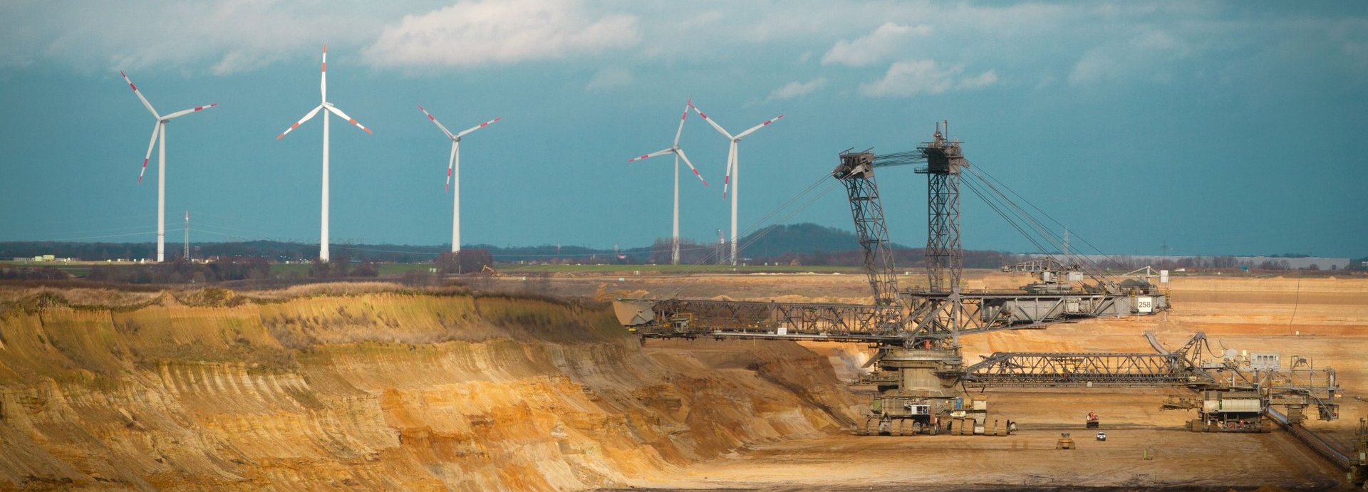 Kohlegrube mit Windrädern am Horizont vor wolkenbehangenem Himmel