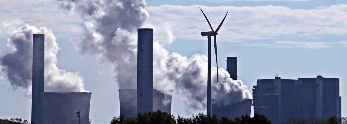 Kohlekraftwerk stößt Qualm am Horizont aus mit einem einzigen Windrad dazwischen