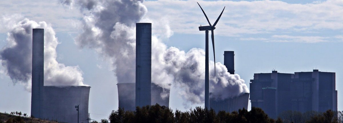 Kohlekraftwerk stößt Qualm am Horizont aus mit einem einzigen Windrad dazwischen