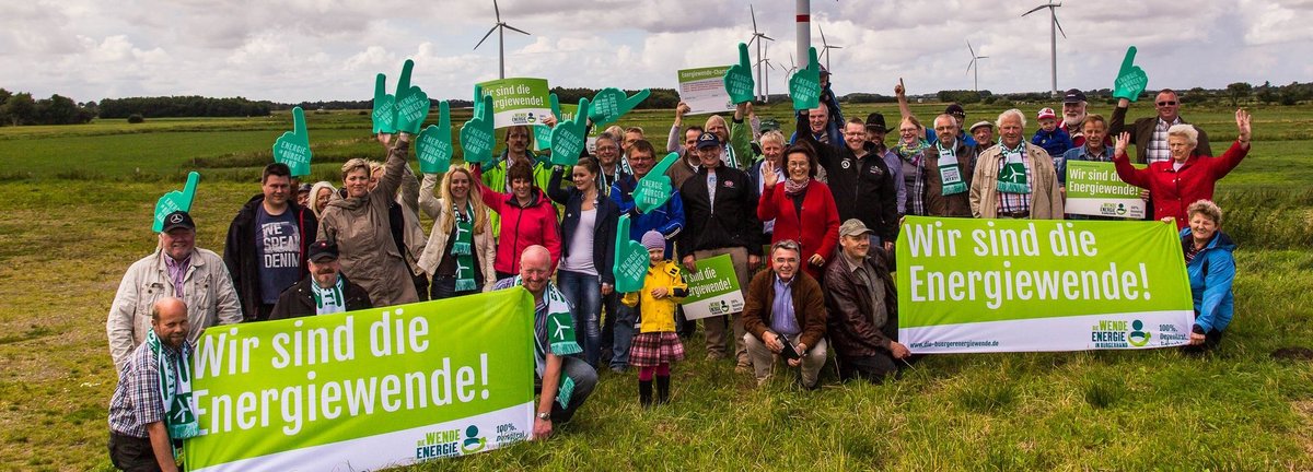 Menschengruppe mit Wir sind Energiewende Schildern auf einem Feld vor Windrädern