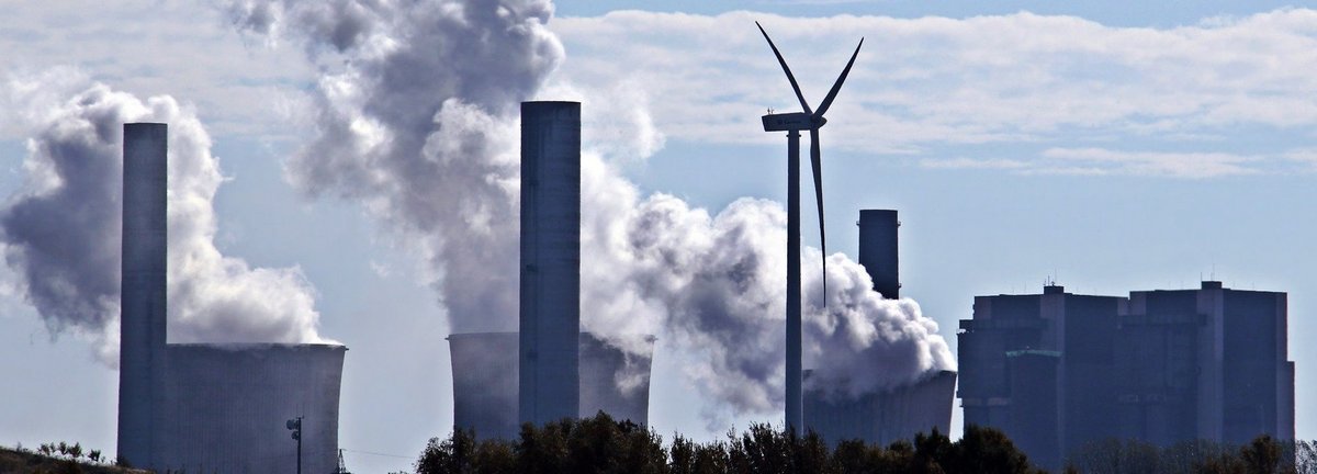 Kohlekraftwerk stößt Qualm am Horizont aus mit einem einzigen Windrad dazwischen