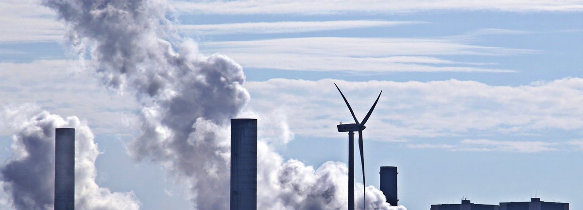 Kohlekraftwerk stößt Qualm am Horizont aus mit einem einzigen Windrad dazwischen