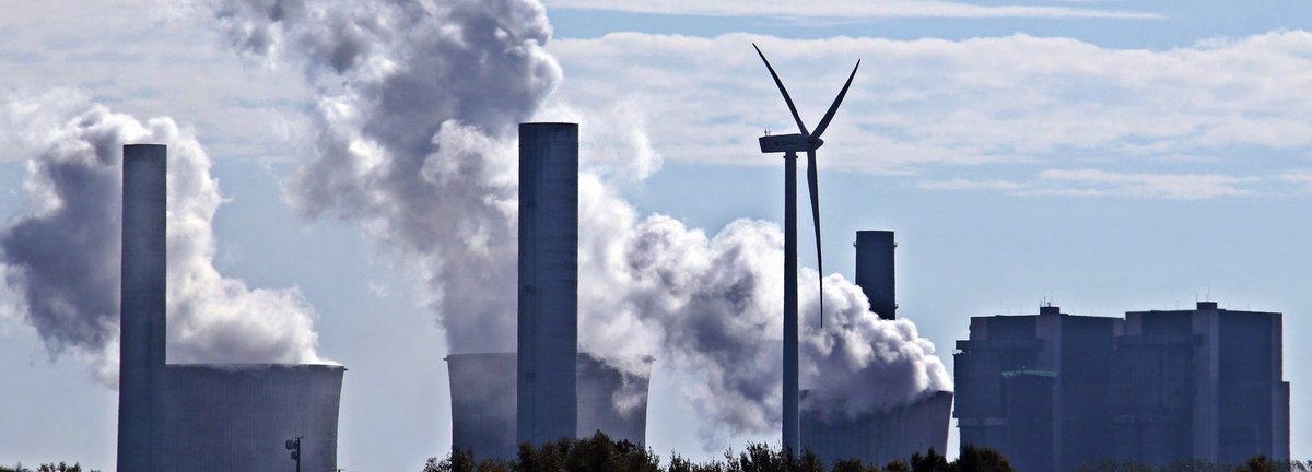 Kohlekraftwerk stößt Qualm am Horizont aus mit einem einzigen Windrad dazwischen
