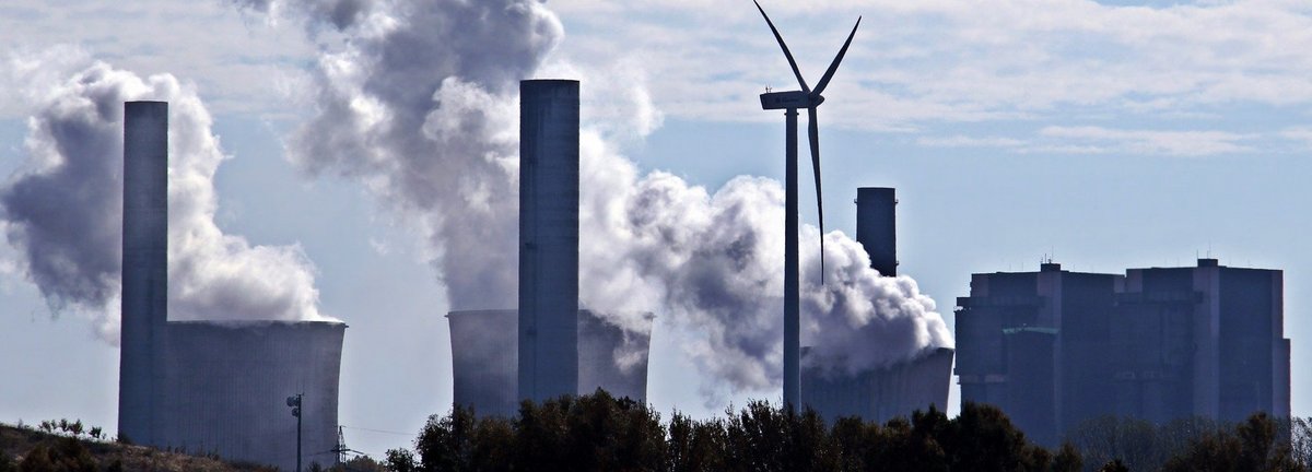 Kohlekraftwerk stößt Qualm am Horizont aus mit einem einzigen Windrad dazwischen