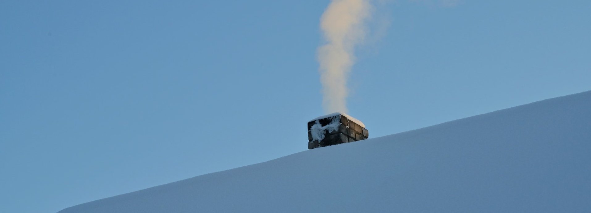 Rauchender Schornstein auf von Schnee bedecktem Dach