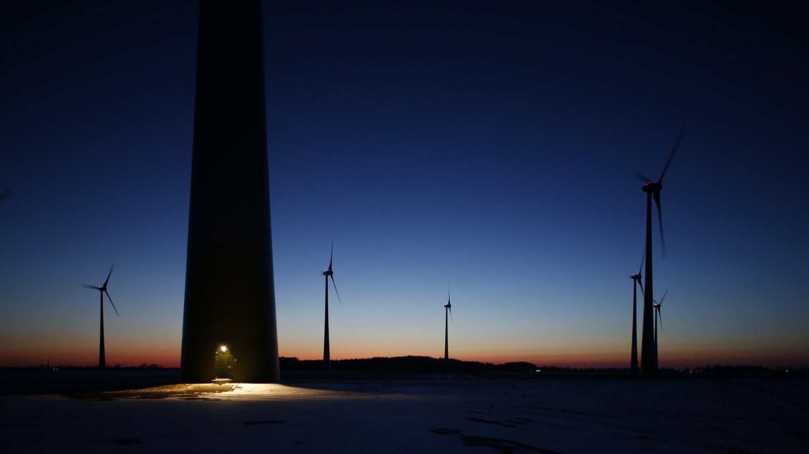 Windrad bei Nacht mit beleuchtetem Eingang, Silhouetten weiter Windräder im Hintergrund