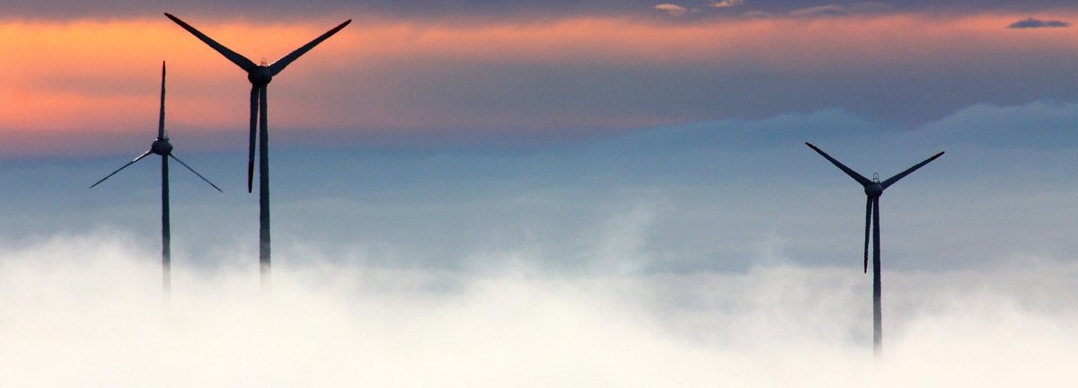 Windräder ragen aus Wolken hervor vor dunkelblauem und orangenem Hintergrund