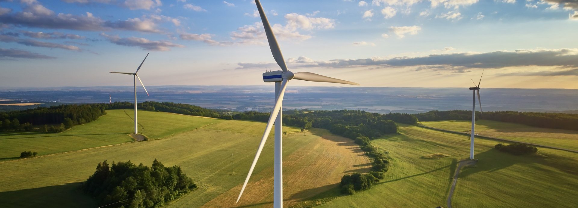 Drohnenfoto mehrerer Windräder auf einem Feld mit wolkigem Himmel