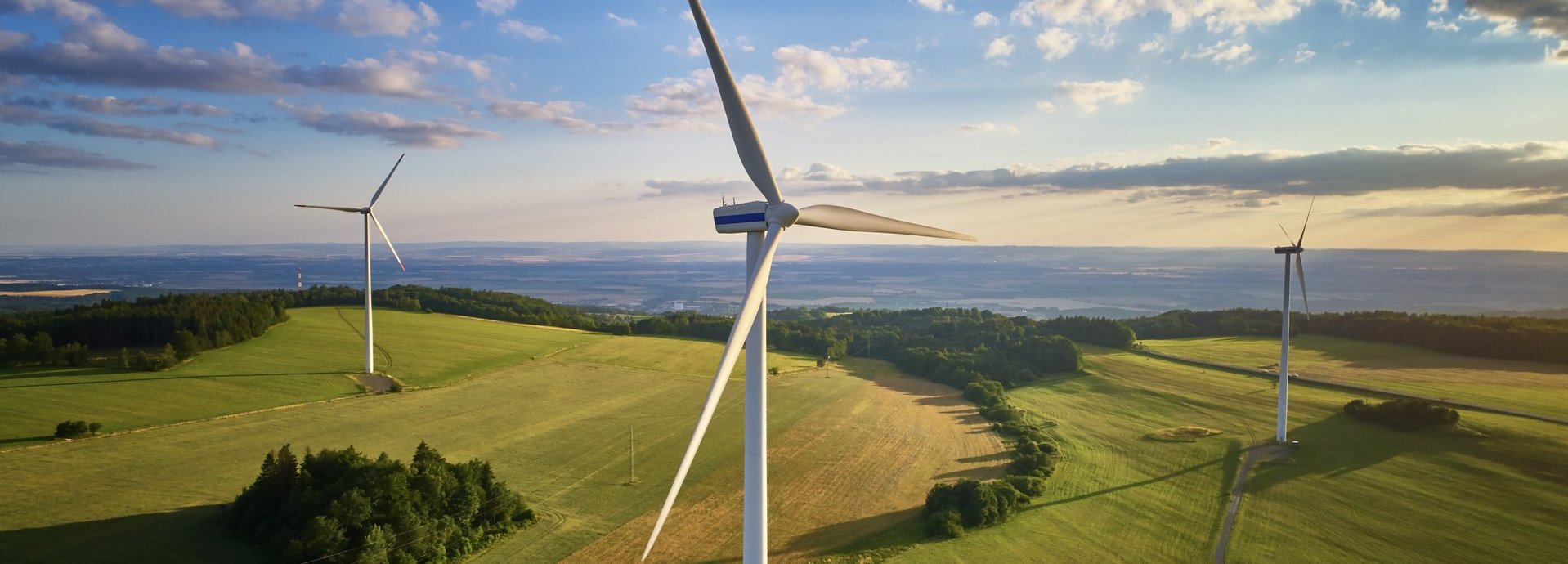 Beschreibung: Drohnenfoto mehrerer Windräder auf einem Feld mit wolkigem Himmel
