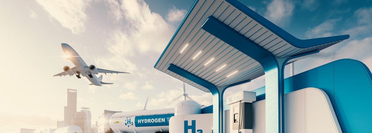 Bildbeschreibung: Wasserstofftankstelle mit LKW, Jet und Stadt im Hintergrund