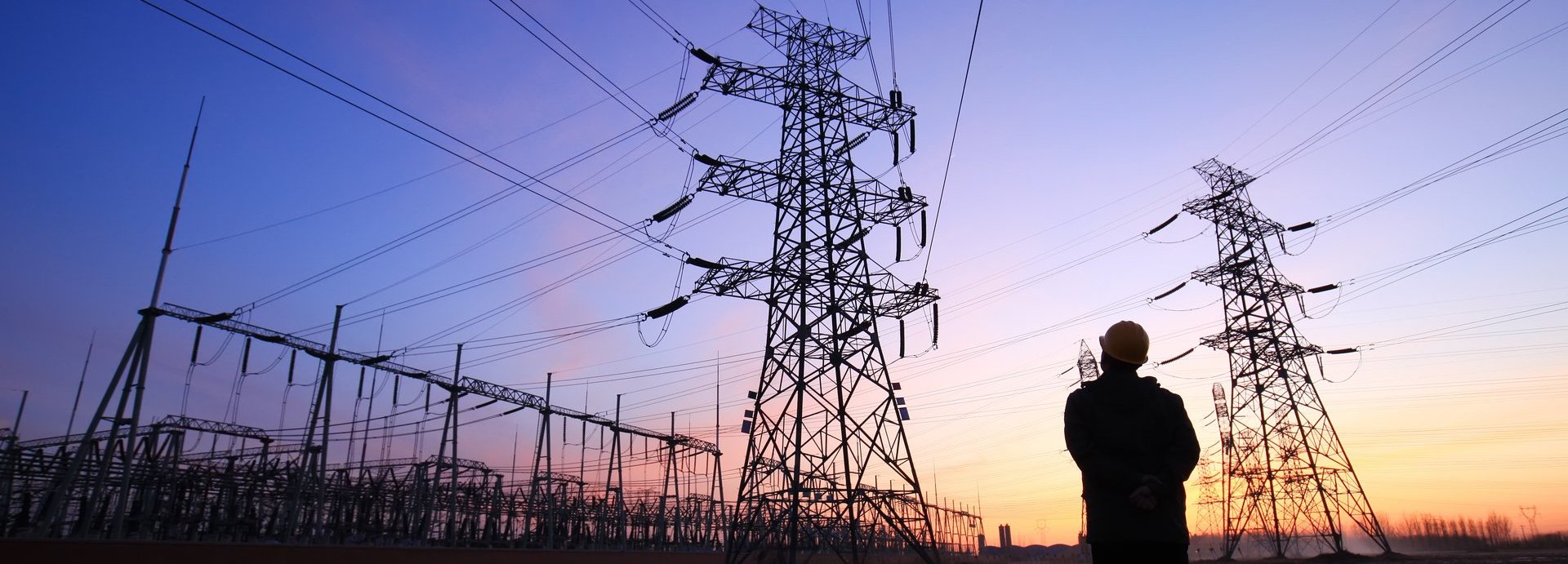 Beschreibung: Ein Arbeiter steht bei Sonnenuntergang vor mehreren Stromleitern