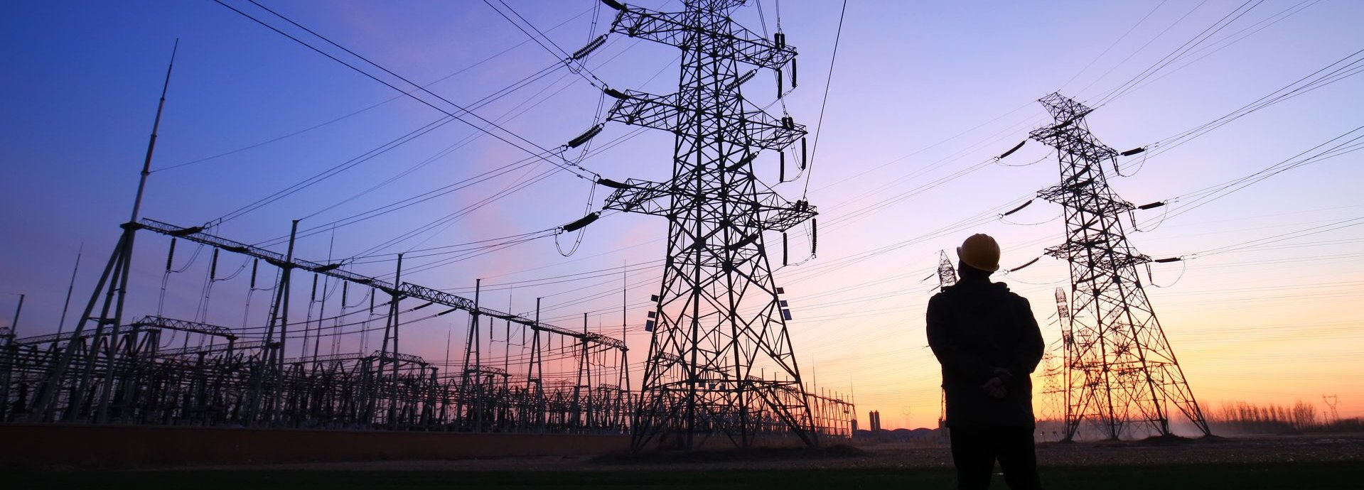 Ein Arbeiter steht bei Sonnenuntergang vor mehreren Stromleitern