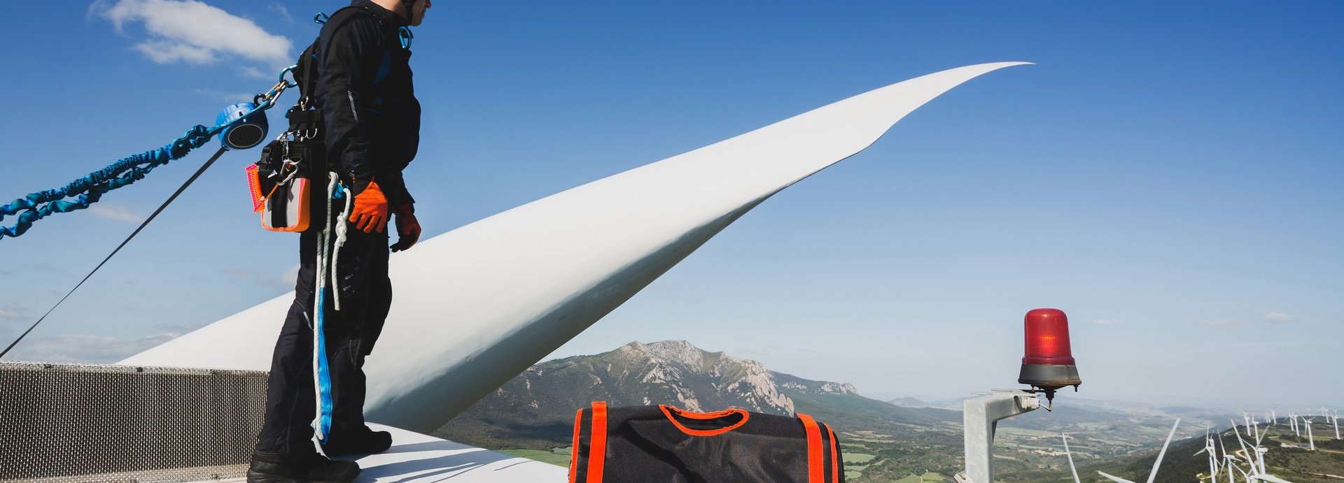 Ingenieur, der oben auf einer Windkraftanlage arbeitet, mit Schutzhandschuhen, Geschirr und Sicherheitsseilen.