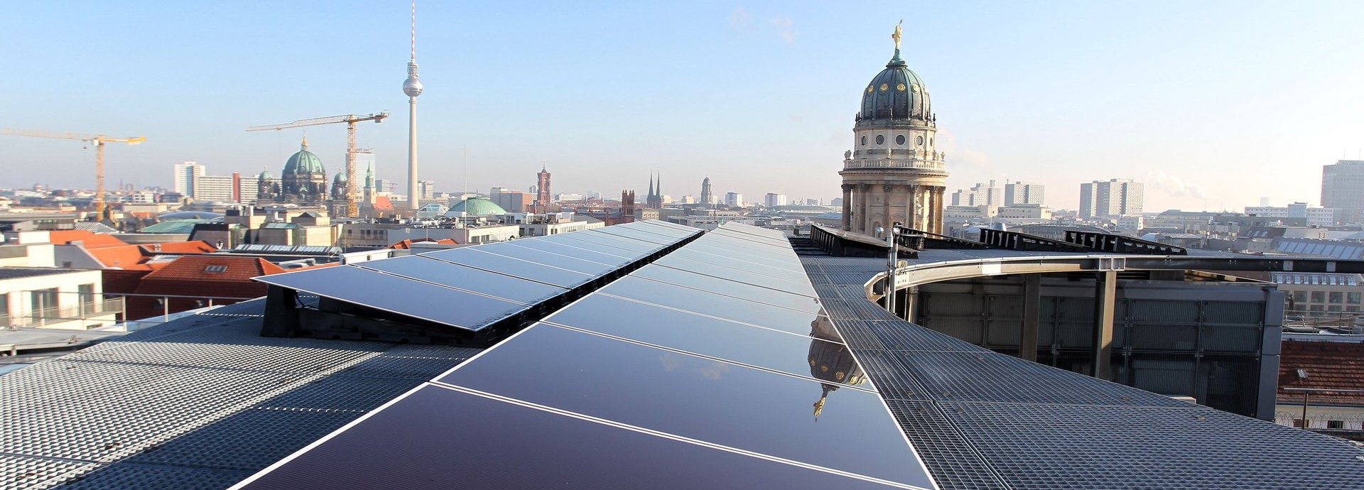 Solarzellen auf einem Dach in Berlin mit dem Fernsehturm am Horizont und blauem Himmel