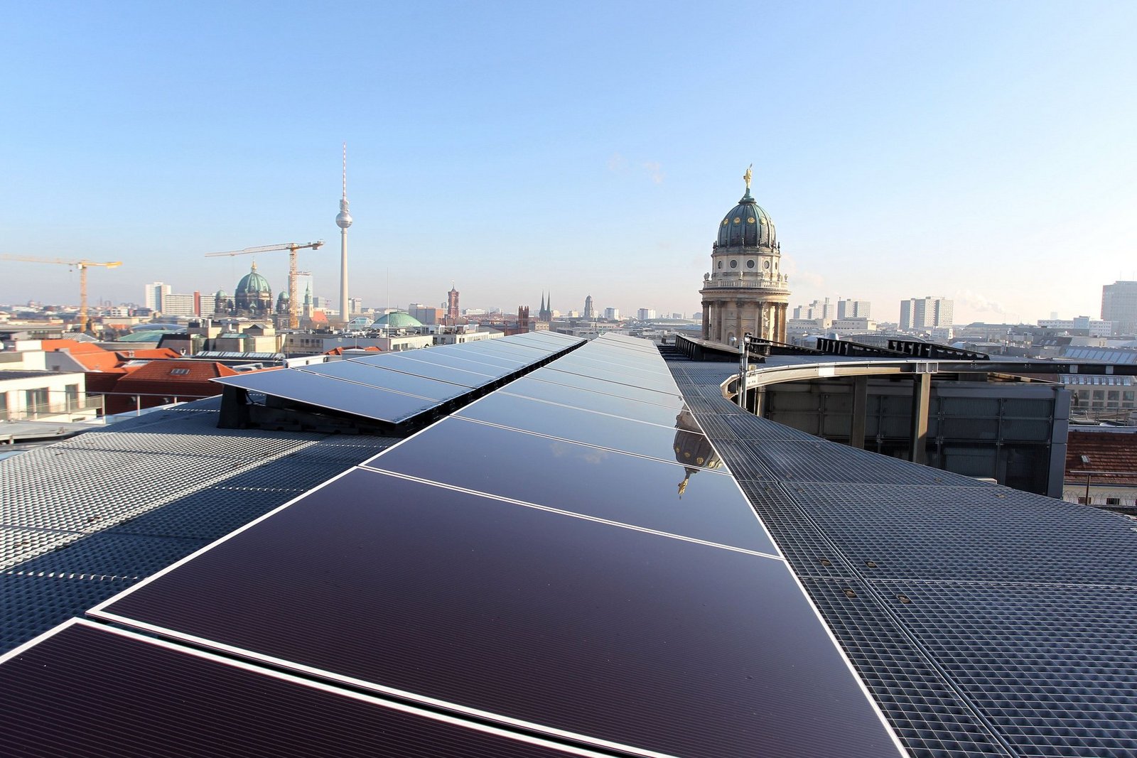 Solarzellen auf einem Dach in Berlin mit dem Fernsehturm am Horizont und blauem Himmel