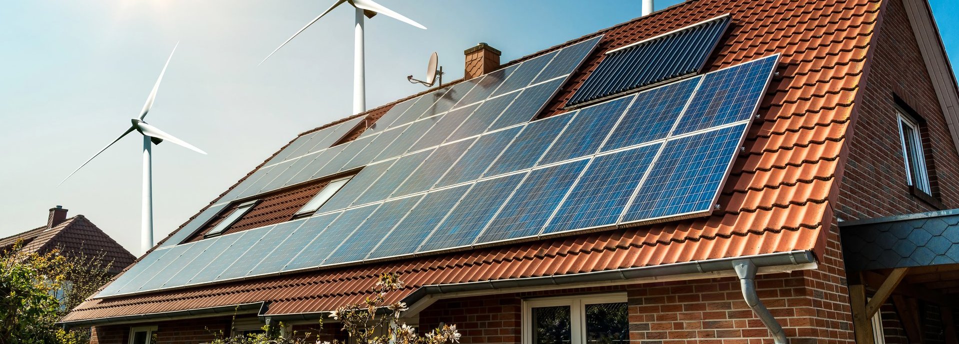 Solarkollektoren auf einem roten Dach mit Sonne und Windrädern im Hintergrund