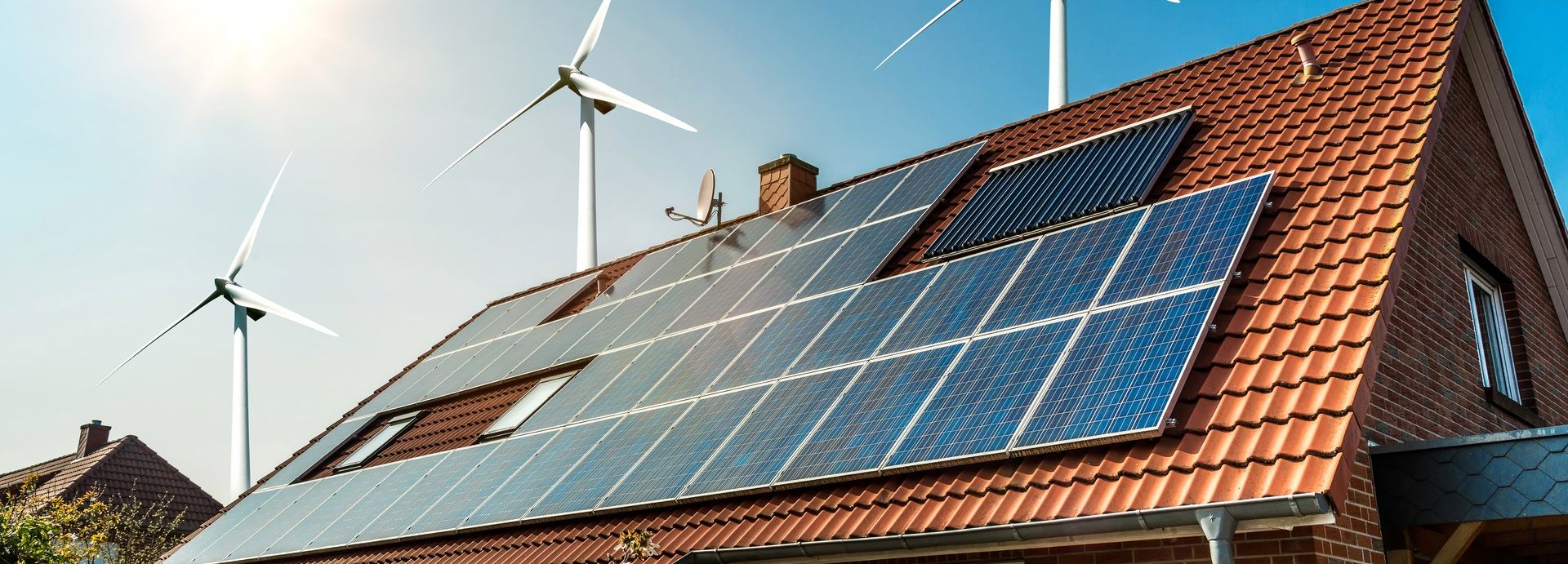 Solarkollektoren auf einem roten Dach mit Sonne und Windrädern im Hintergrund