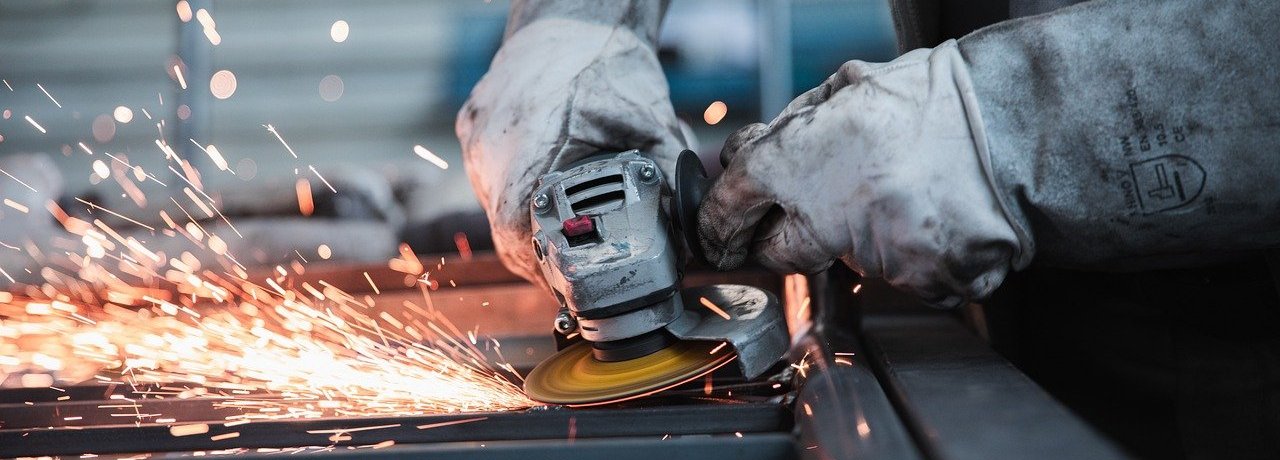 Beschreibung: Nahaufnahme von Händen in Arbeiterhandschuhen bei Schleifarbeit und dabei sprühen Funken