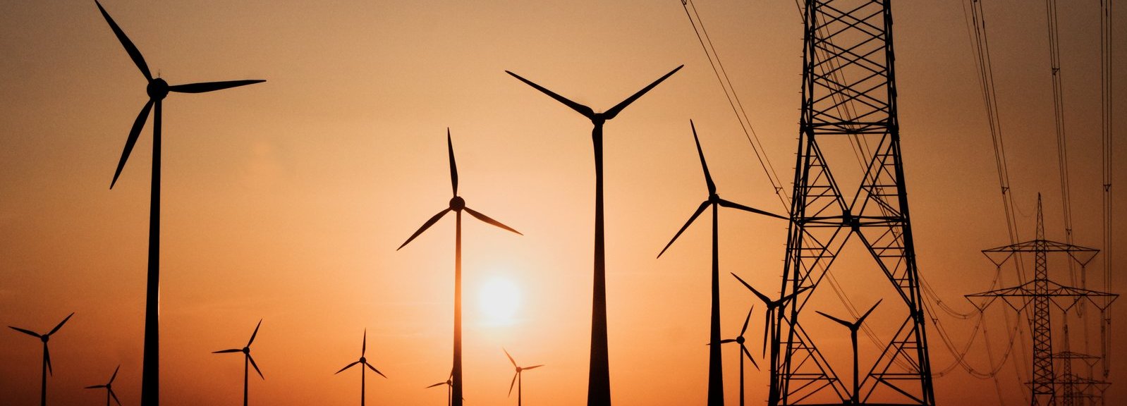 Stromtrasse mit Windrädern vor Sonnenuntergang im Hintergrund