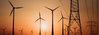 Stromtrasse mit Windrädern vor Sonnenuntergang im Hintergrund