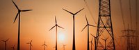 Stromtrasse mit Windrädern vor Sonnenuntergang im Hintergrund