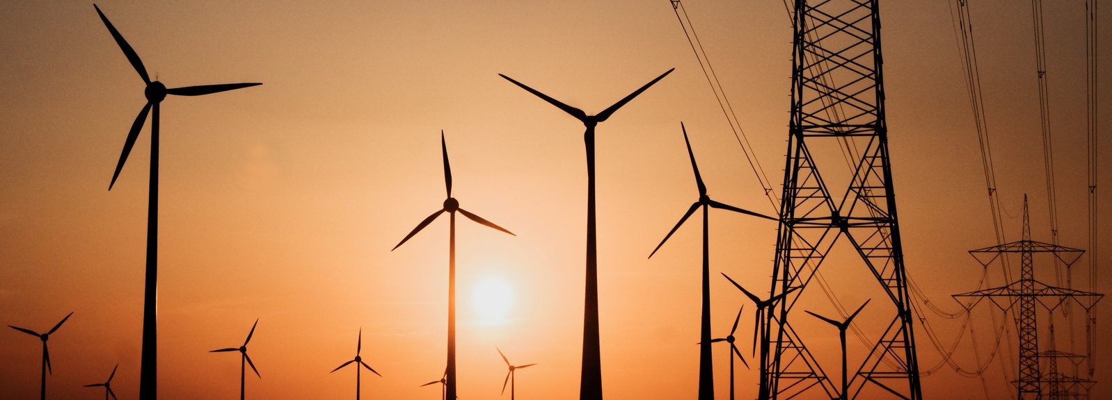 Stromtrasse mit Windrädern vor Sonnenuntergang im Hintergrund