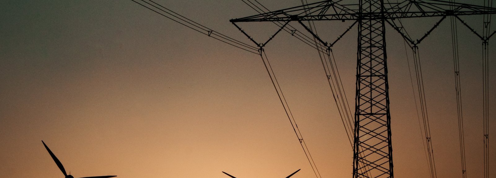 Beschreibung: Stromtrasse mit Windrädern vor Sonnenuntergang im Hintergrund