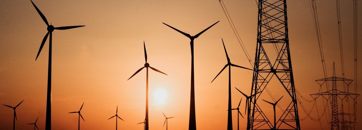 Stromtrasse mit Windrädern vor Sonnenuntergang im Hintergrund