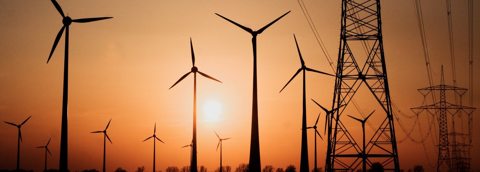 Stromtrasse mit Windrädern vor Sonnenuntergang im Hintergrund