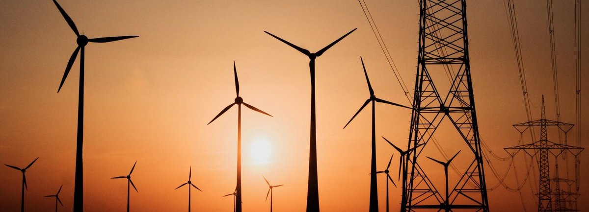 Stromtrasse mit Windrädern vor Sonnenuntergang im Hintergrund