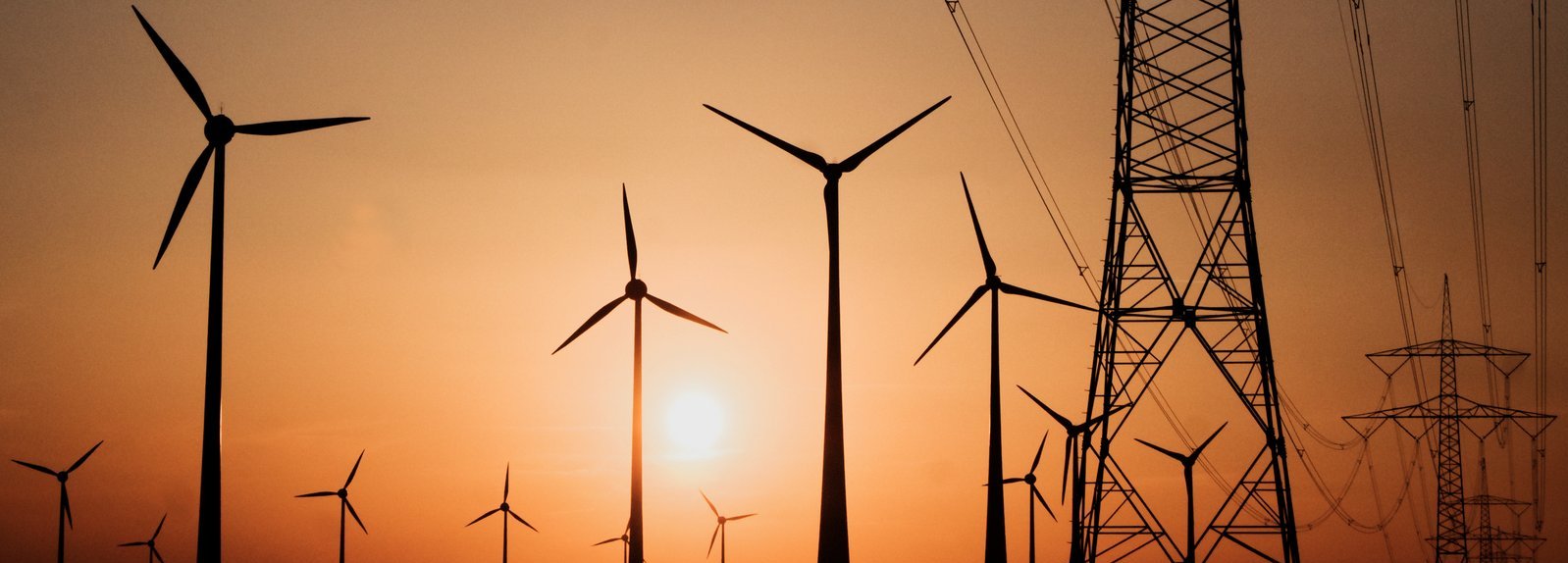 Stromtrasse mit Windrädern vor Sonnenuntergang im Hintergrund