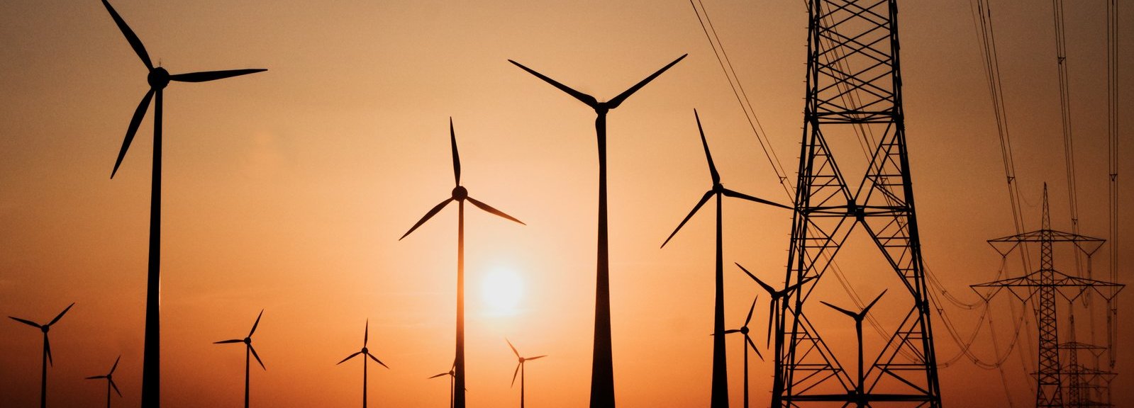 Stromtrasse mit Windrädern vor Sonnenuntergang im Hintergrund