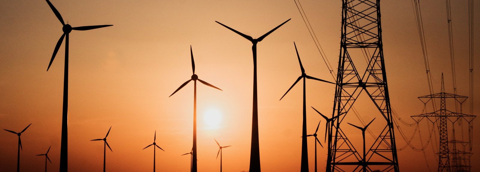 Stromtrasse mit Windrädern vor Sonnenuntergang im Hintergrund