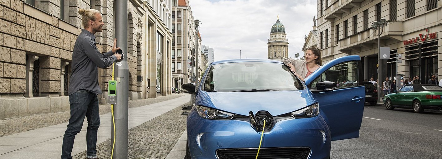 Ein Mann in einem Stadtgebiet lädt sein blaues E-Auto an einer Laterne