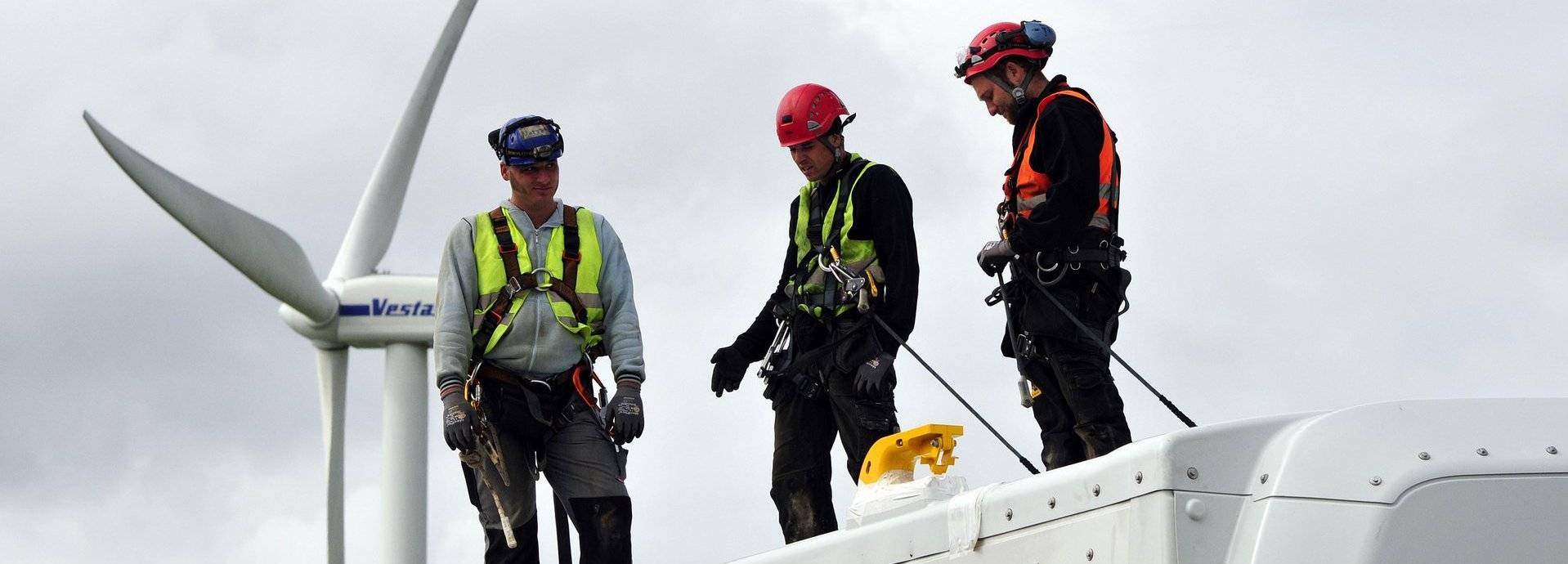 Drei Arbeiter mit Warnwesten und Helmen stehen auf einem Windrad und besprechen sich