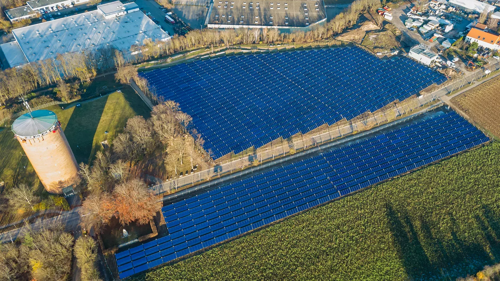 Vogelaufnahme eines großen Solarfelds auf einem Feld umgeben von Gebäuden